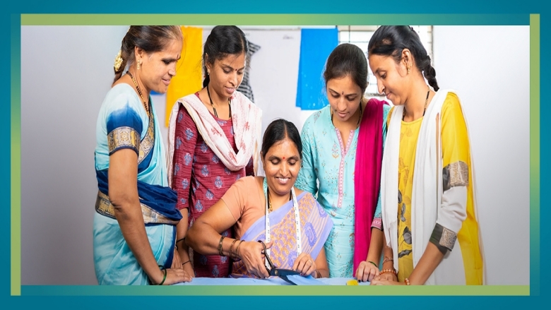 A female trainer instructs a group of female students on how to cut fabric at a training center