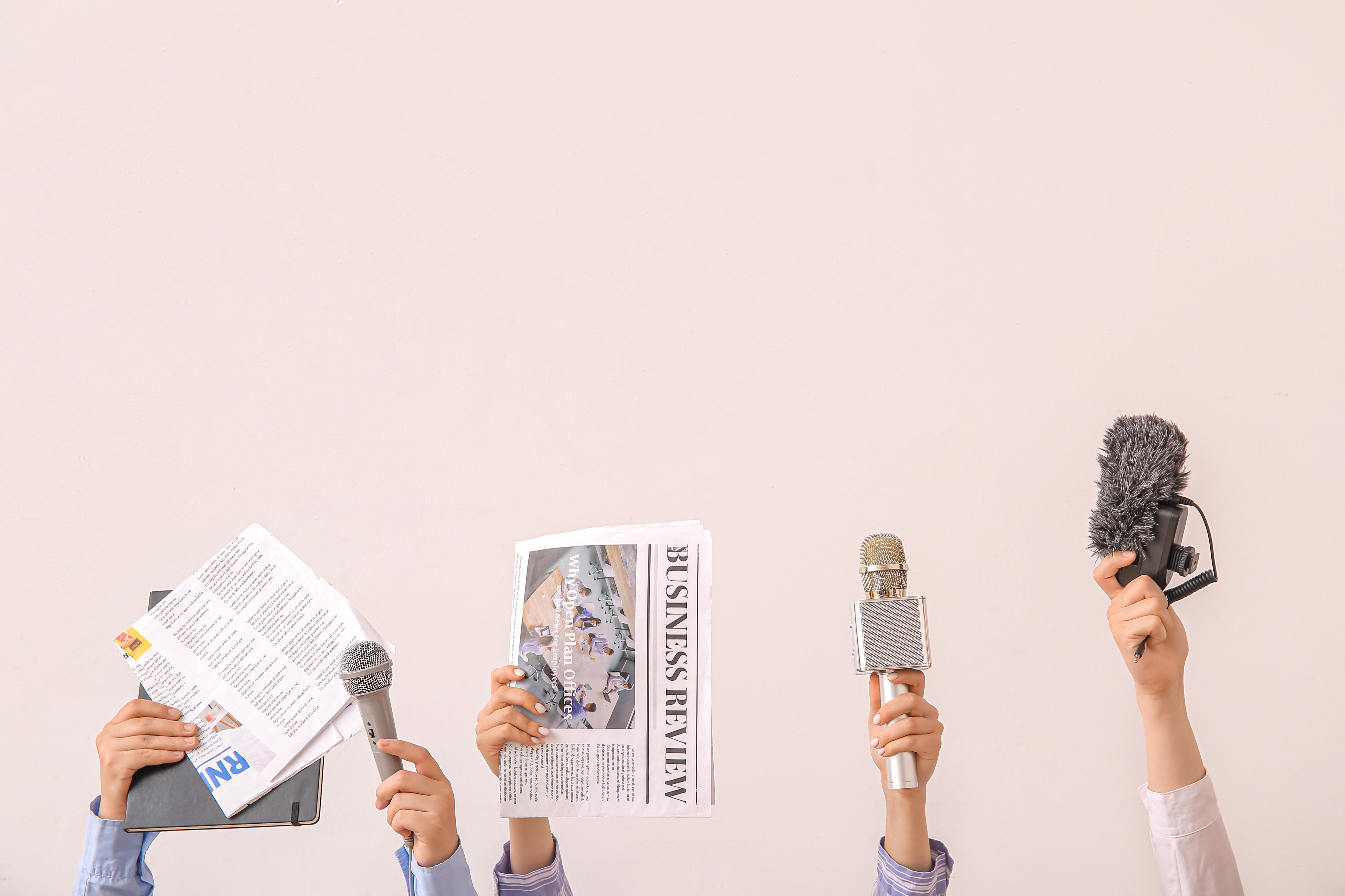 Female hands with newspapers and microphones on light background